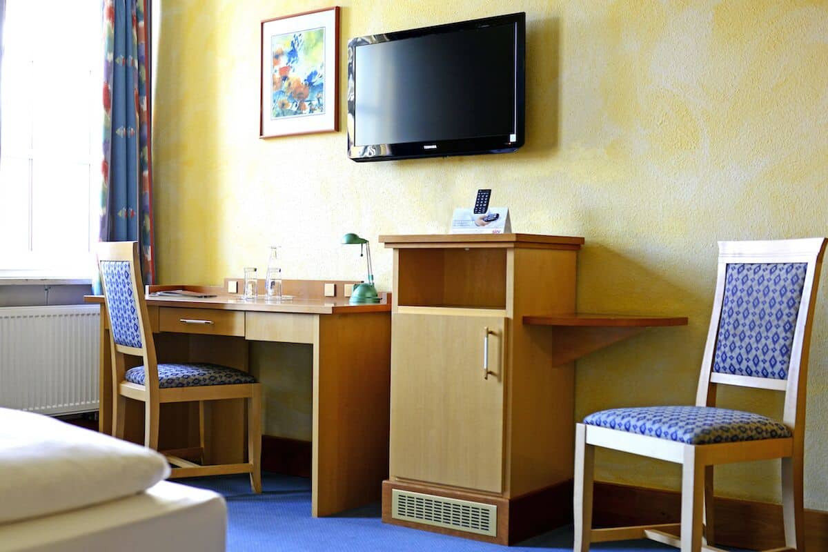 Habitación de hotel con cama, escritorio, silla, televisor y ventana con cortinas.
