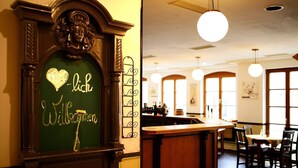 A restaurant interior with a green sign reading "Willkommen" and a heart-shaped decoration. There are wooden tables and chairs, and a bar area with bottles. - Altstadthotel Haßfurt (Hassfurt)