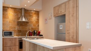 A modern kitchen with a central island, wooden cabinets, a built-in microwave, and a stainless steel range hood. - Contemporary Apartment made of Wood and Stone (Athens)
