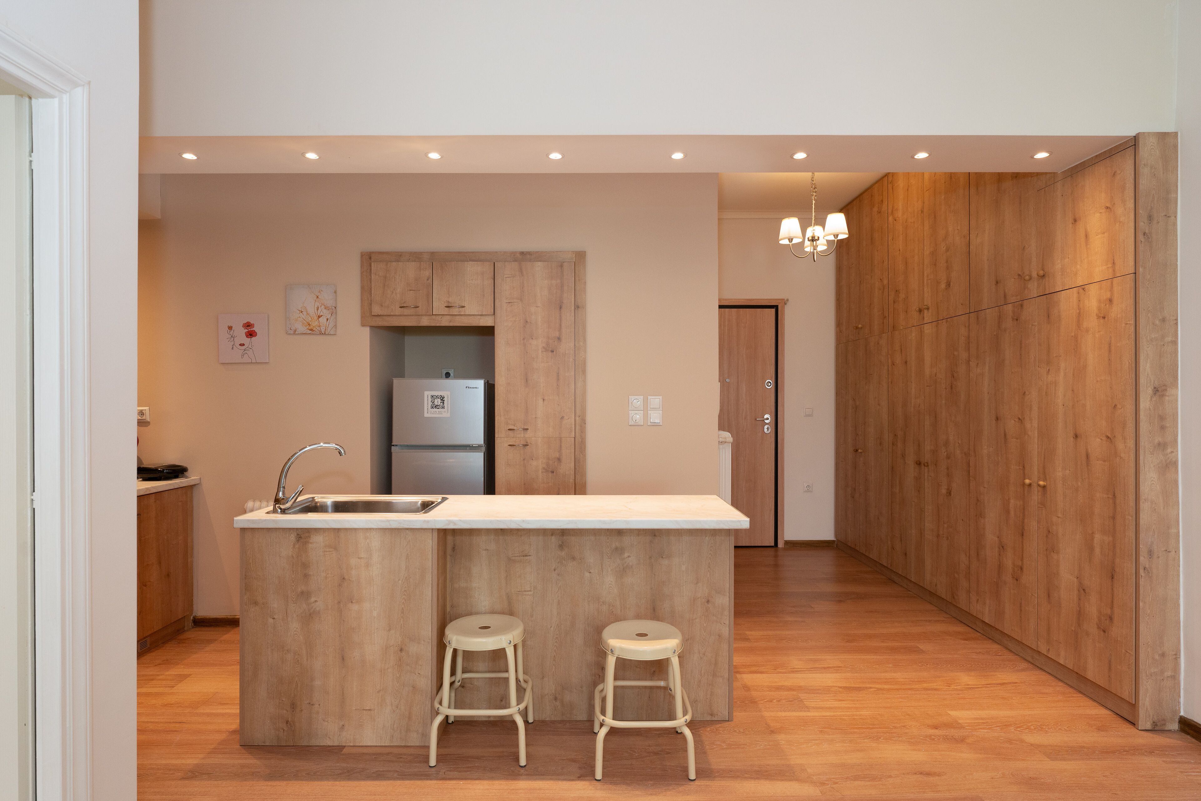 A modern kitchen with wooden cabinets, a central island with stools, a built-in refrigerator, and recessed lighting.