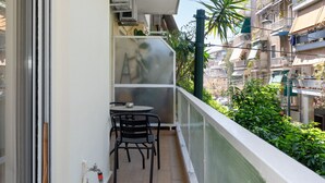 A balcony with a table and chairs, air conditioning units, and a view of neighboring buildings. - Contemporary Apartment made of Wood and Stone (Athens)