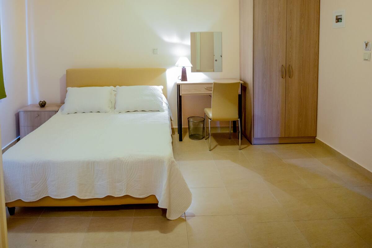 Une chambre à coucher comprenant un lit, un bureau, une chaise, une armoire et un luminaire suspendu.