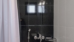 Kylpyhuoneessa on mustilla laatoilla päällystetty suihkuseinä, valkoinen kylpyamme ja valkoinen pesuallas.
