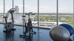 Ein Fitnessstudio mit Trainingsgeräten und großen Fenstern mit Blick auf eine Stadtlandschaft.