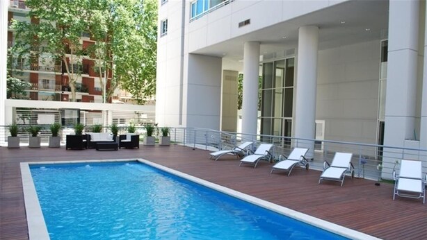 Ein rechteckiger Pool mit Holzterrasse, umgeben von weißen Liegestühlen und Blumentöpfen.