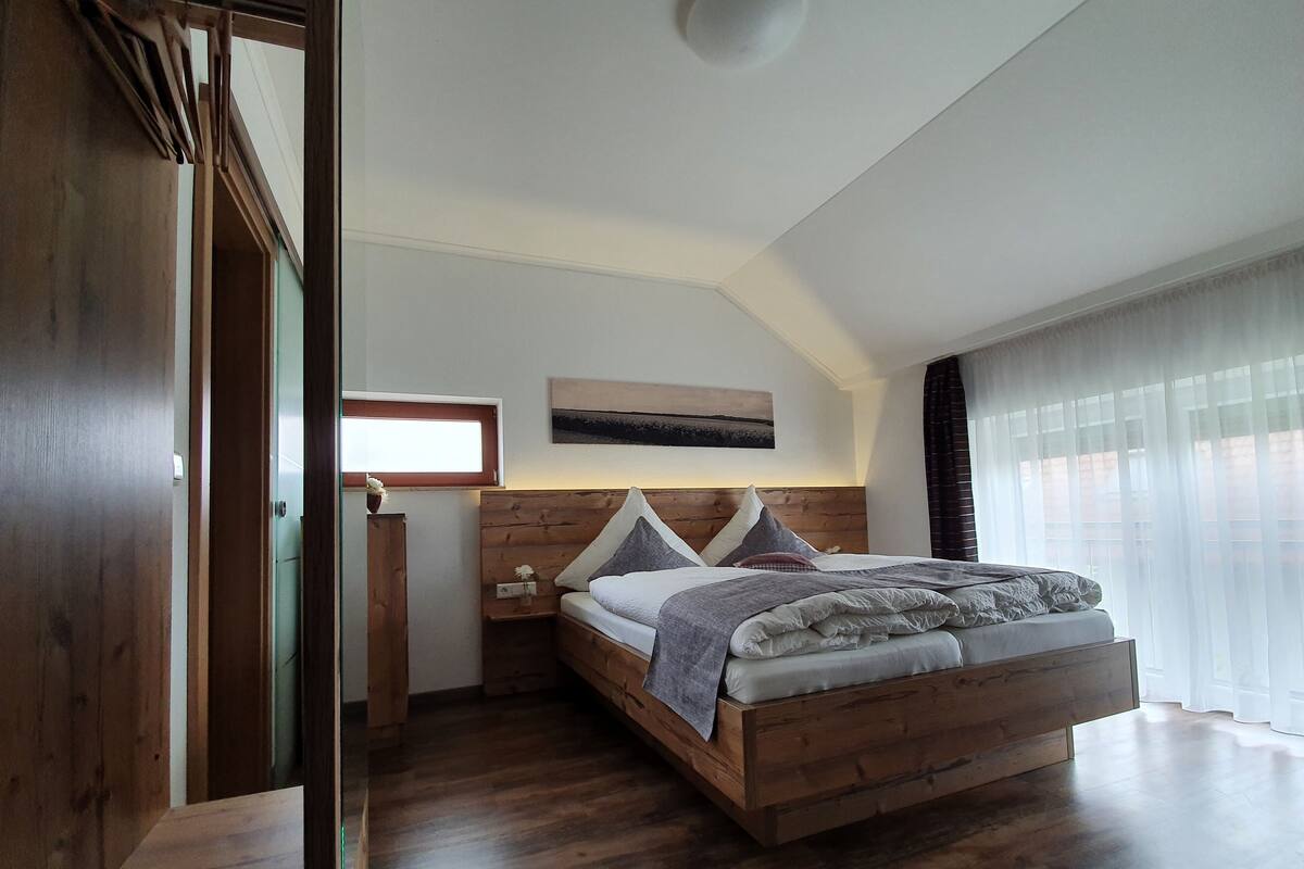 Un dormitorio con una cama de madera, una mesita de noche, una ventana con cortinas y un armario de madera.
