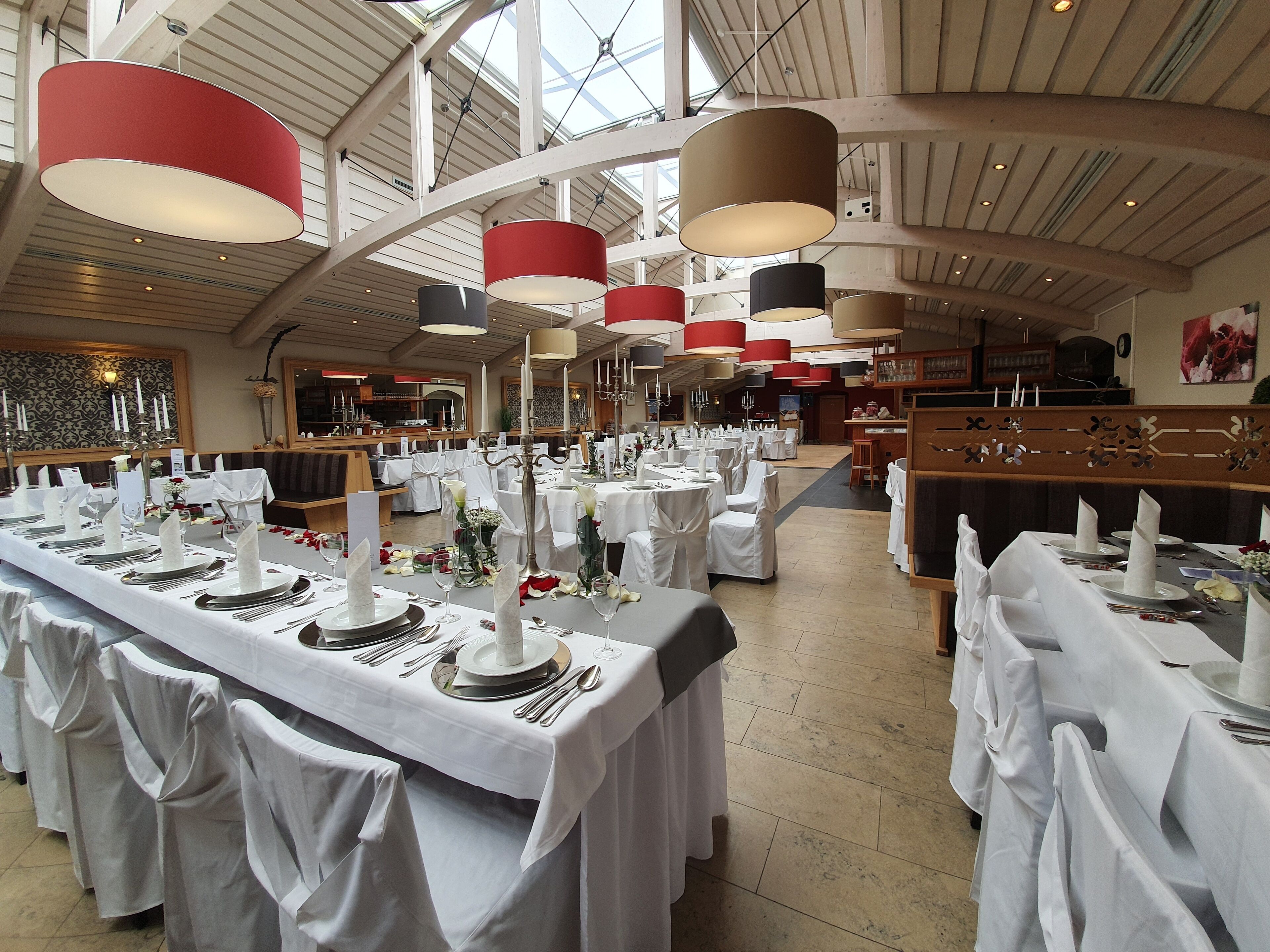 A spacious banquet hall with high ceilings and large pendant lights. Tables are set with white tablecloths and silverware.