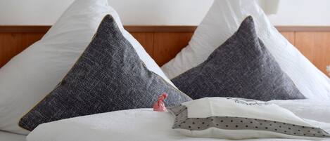 A bed with white and gray pillows, a small pink figurine, and a polka-dotted pillow.