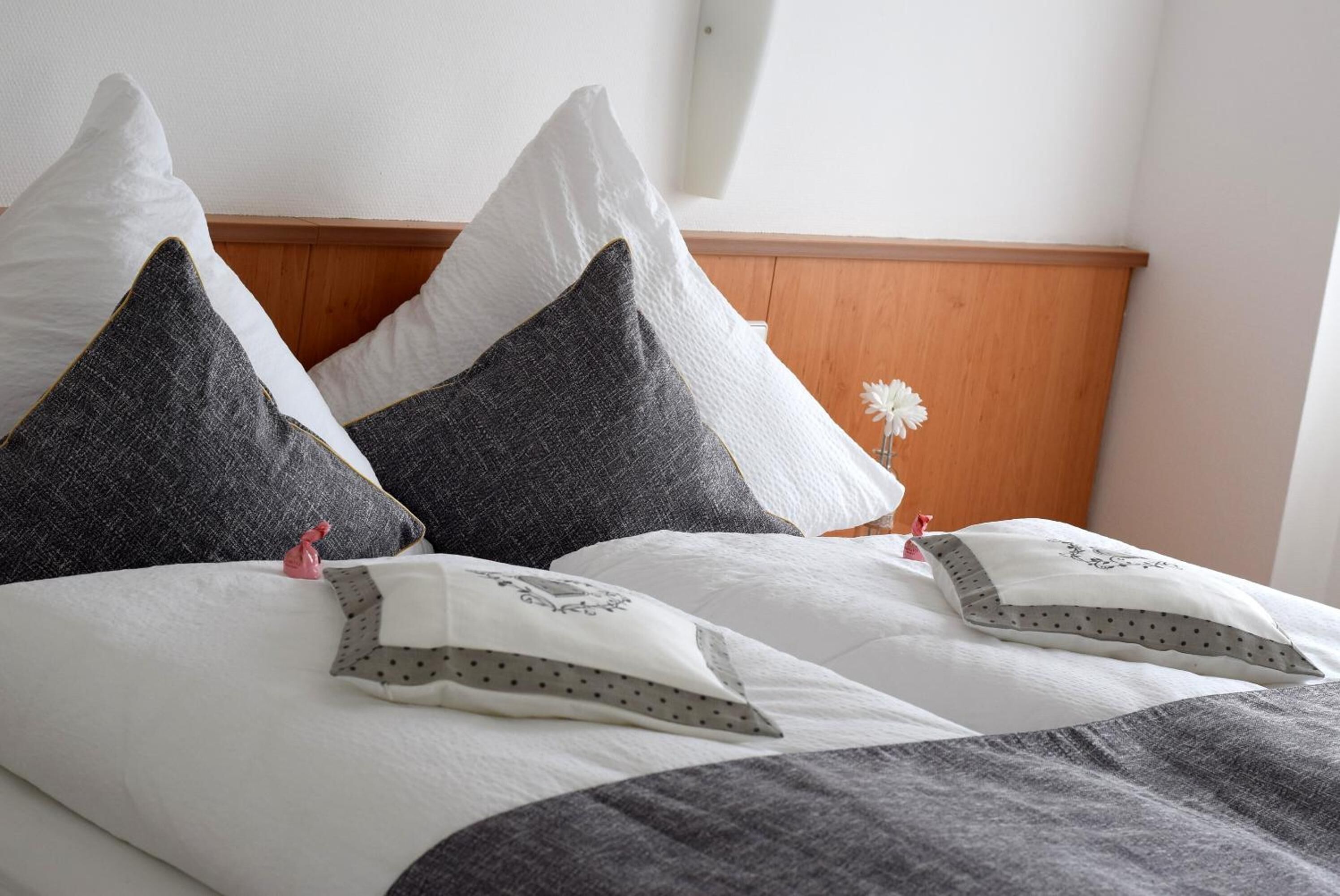 A neatly made bed with white and gray pillows, a wooden headboard, and a small decorative flower.