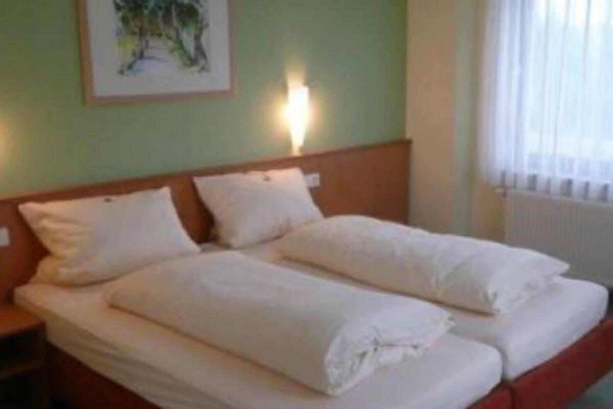 Una cama doble con sábanas blancas, cabecera e imagen enmarcada en la pared.