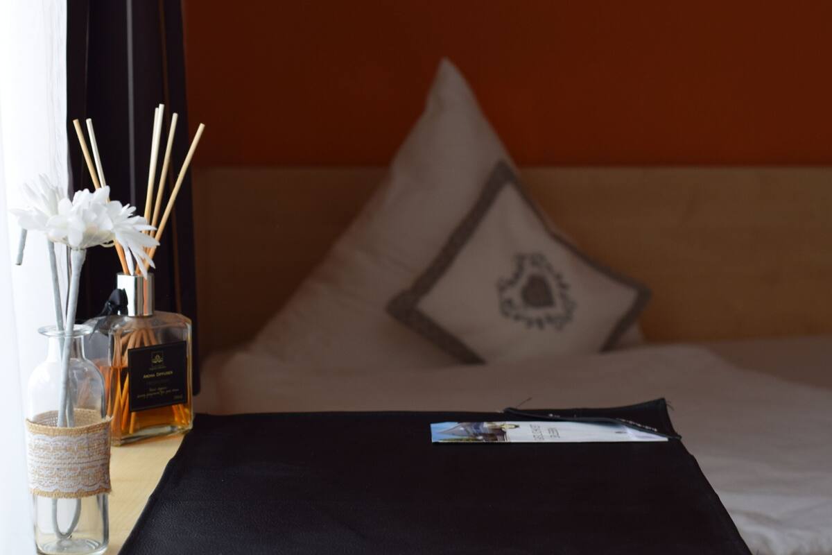 Una habitación de hotel con una cama, una mesita de noche, un frasco de perfume y una revista.
