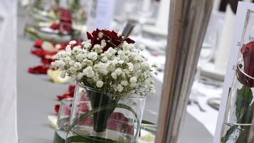 Una larga mesa con jarrones de vidrio transparente que contienen flores y pétalos de rosa, sobre un mantel blanco.
