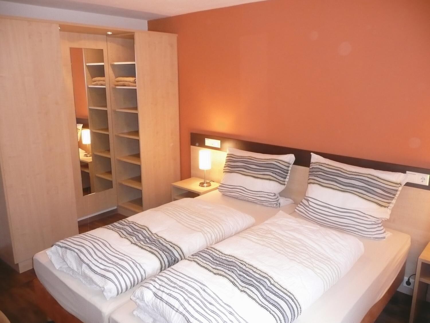 Una cama doble con ropa de cama a rayas, una mesita de noche con lámpara y un armario de madera con estantes.