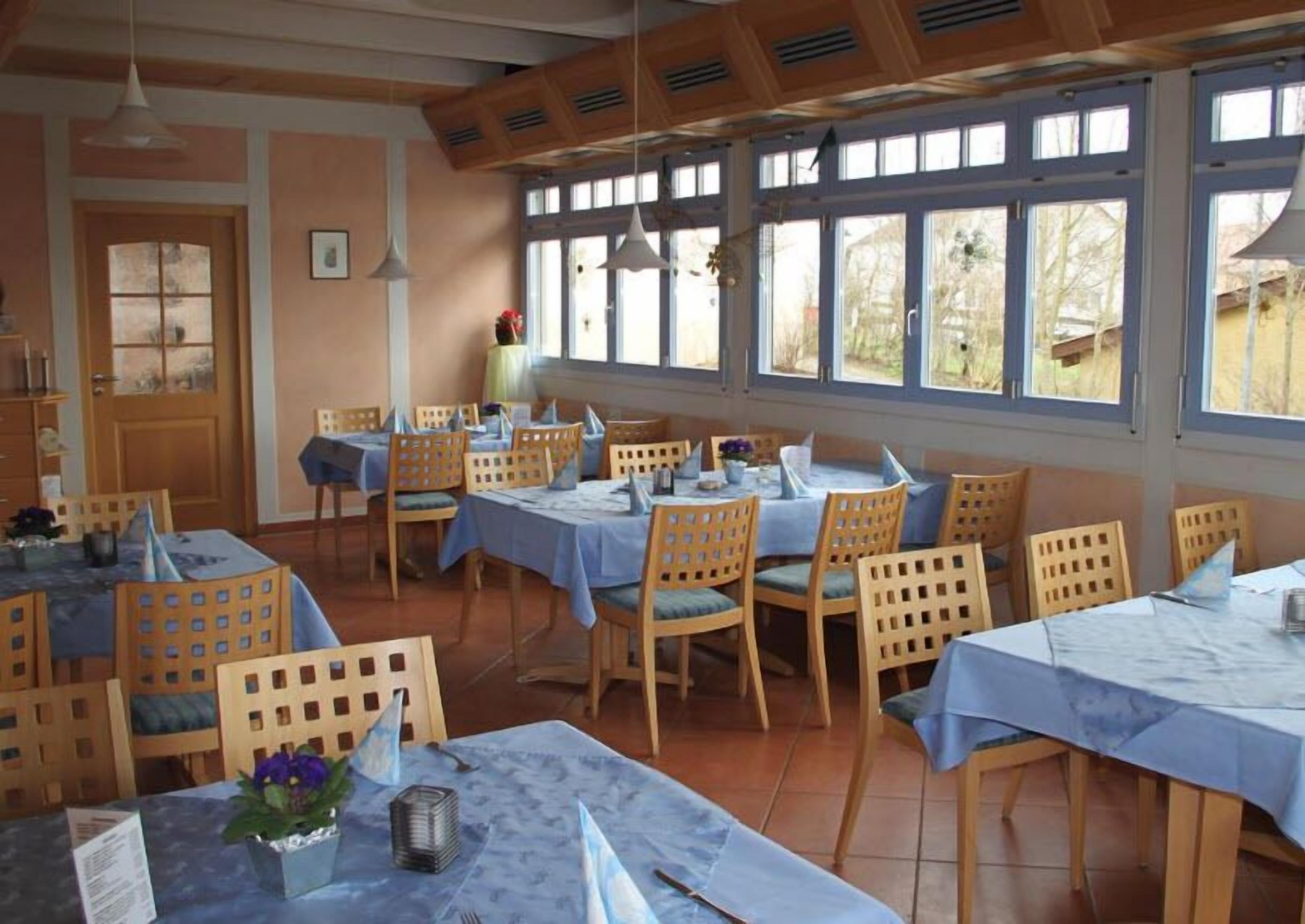 Un comedor con varias mesas y sillas, ventanas amplias y techo de madera.