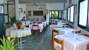 Um restaurante com várias mesas, cada uma disposta com toalhas brancas e cadeiras.
