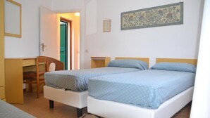Quarto com duas camas de solteiro, uma escrivaninha e uma cadeira.