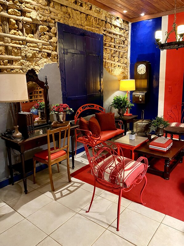 Una habitación con pared de piedra, puerta azul, escritorio de madera, sofá rojo y silla roja.