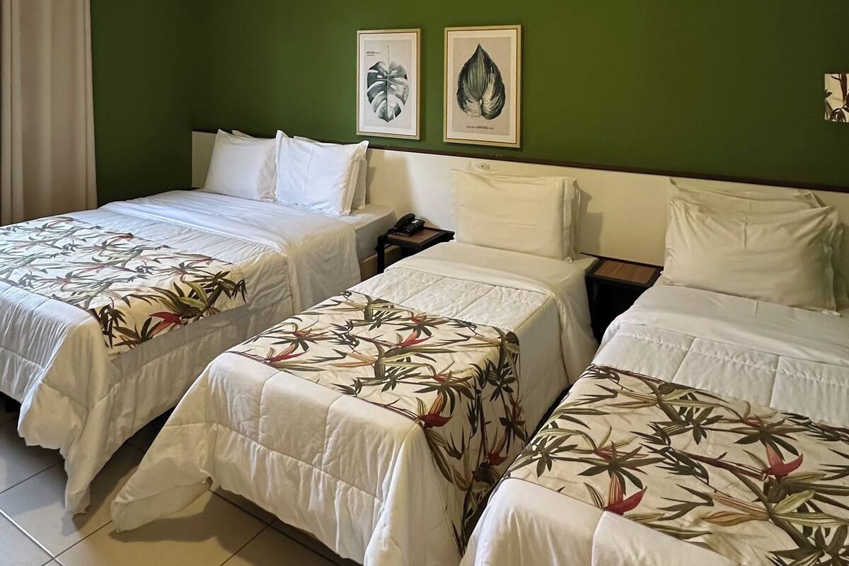 A hotel room with two beds, green walls, and two framed botanical prints.