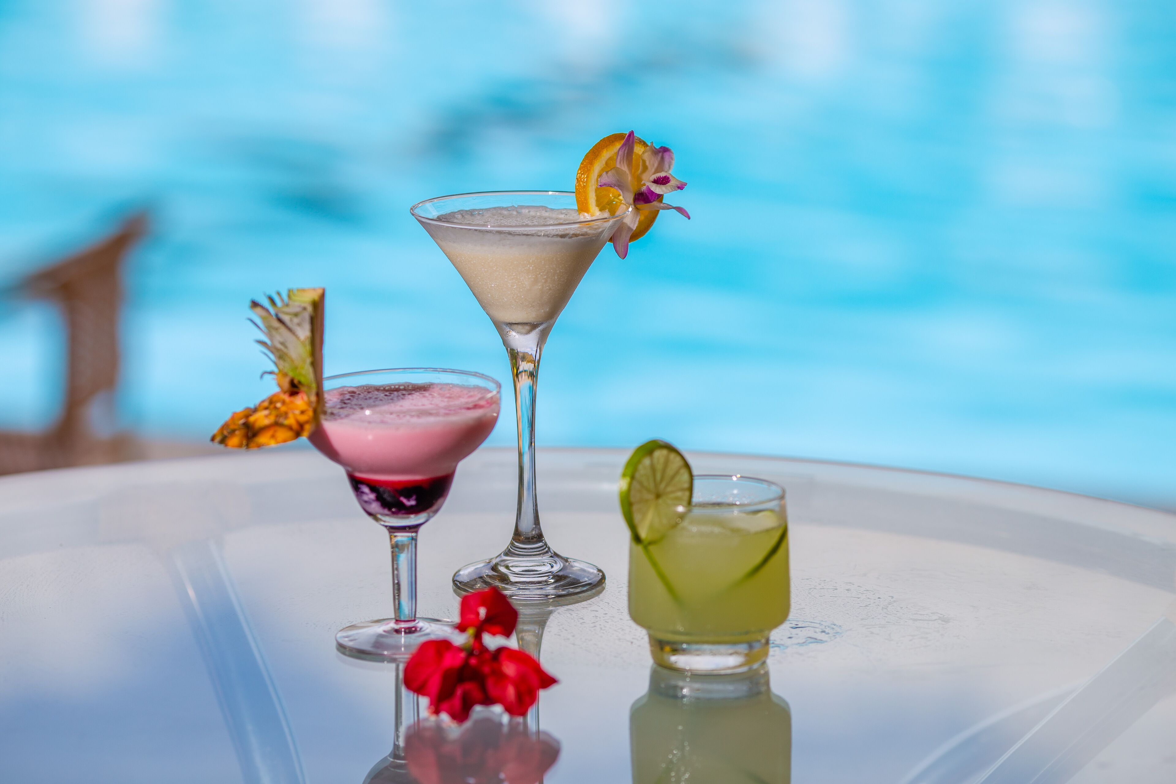 Three cocktails on a table with a pool in the background.