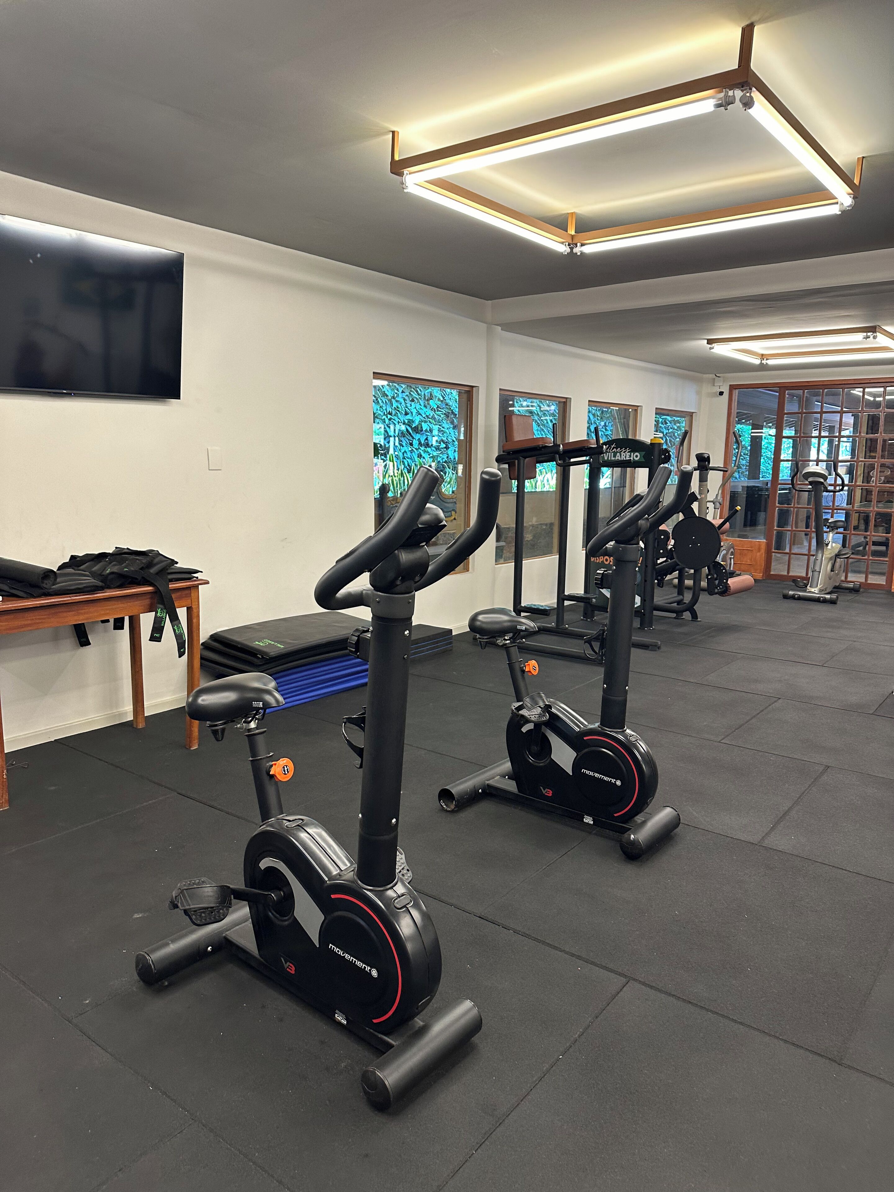 Uma academia com bicicletas ergométricas, um banco e equipamentos de exercícios.