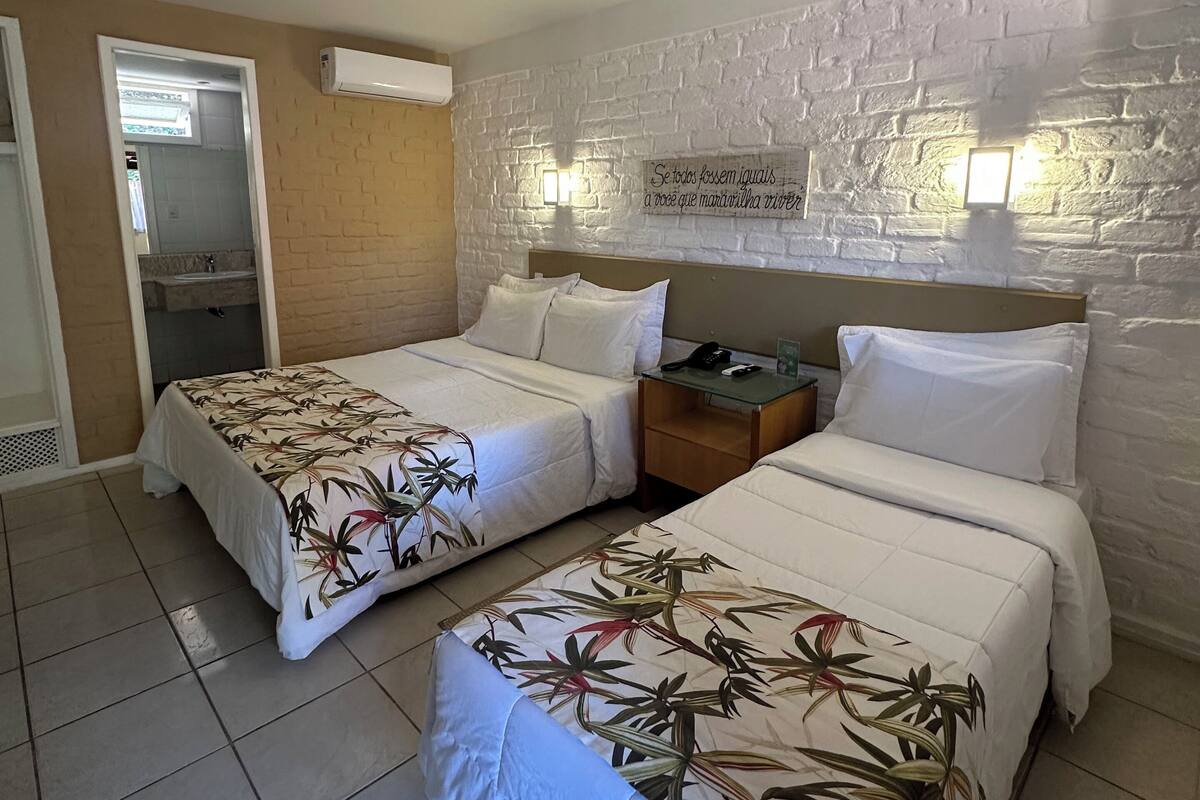 A hotel room with two beds, a brick wall, a mirror, and a small table with a phone.