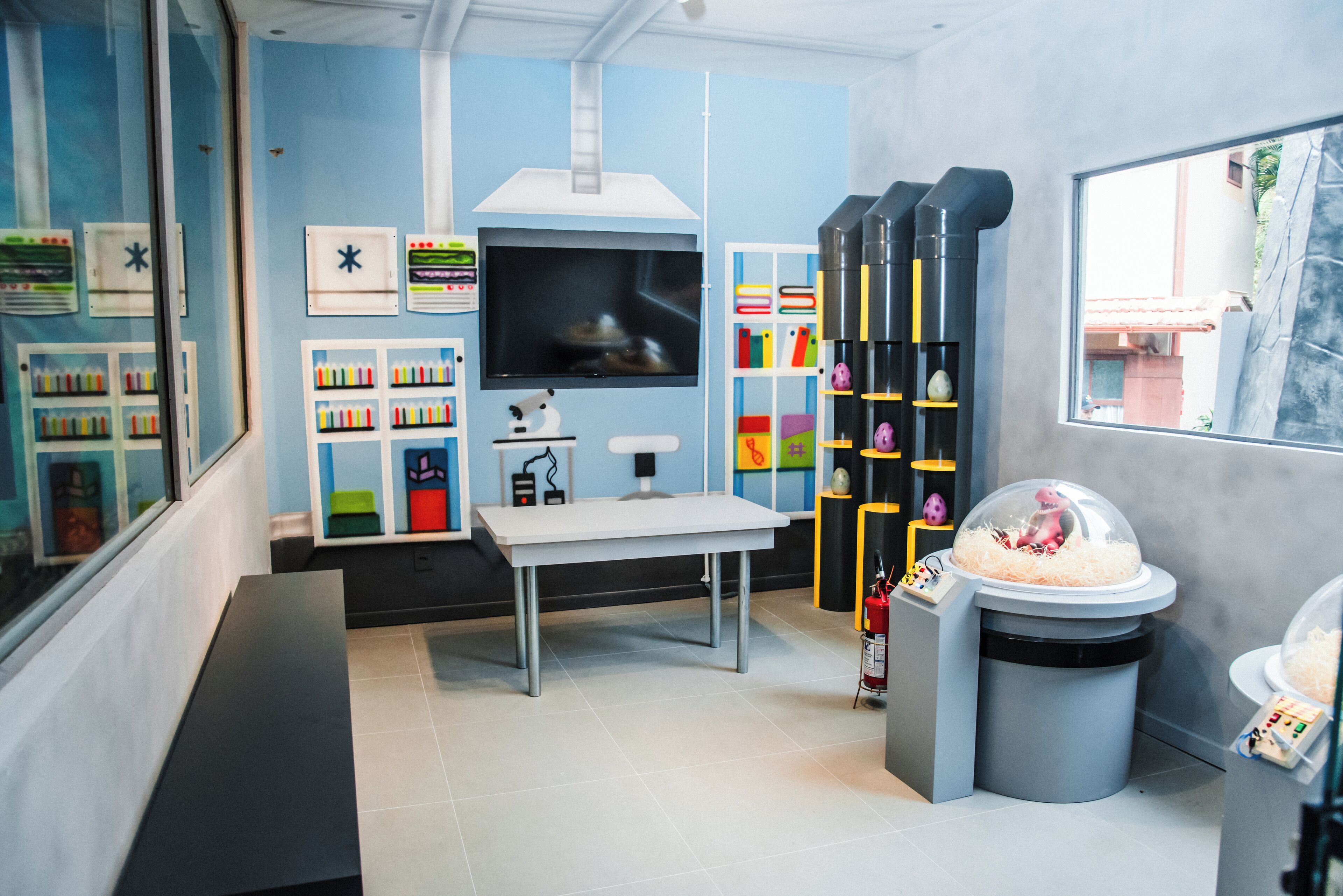 A room with a white table, a TV, shelves with colorful items, and a trash bin with a dome cover.