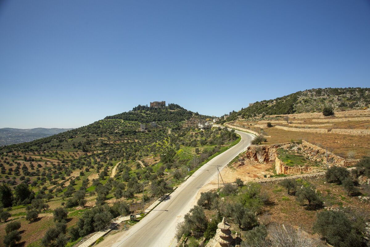 A winding road through a hilly landscape with a castle on a hill.