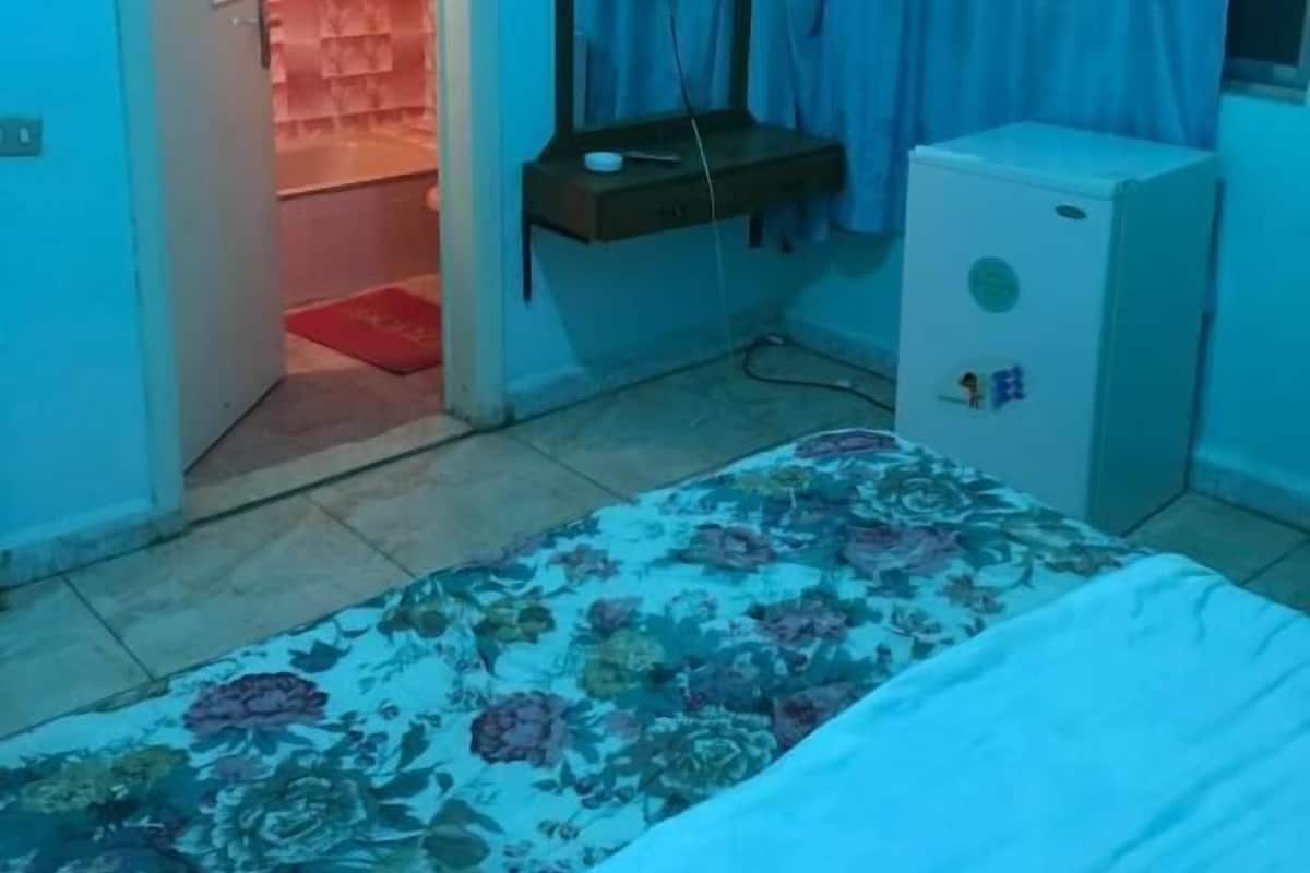 Ett sovrum med en säng, ett litet kylskåp, en tv och ett badrum med duschdraperi.