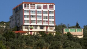 A multi-story building with a red and white facade, surrounded by dense greenery. - Ajloun Hotel (Ajloun)
