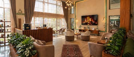 A spacious living room with a large TV, comfortable seating, a wooden reception desk, and a bookshelf.