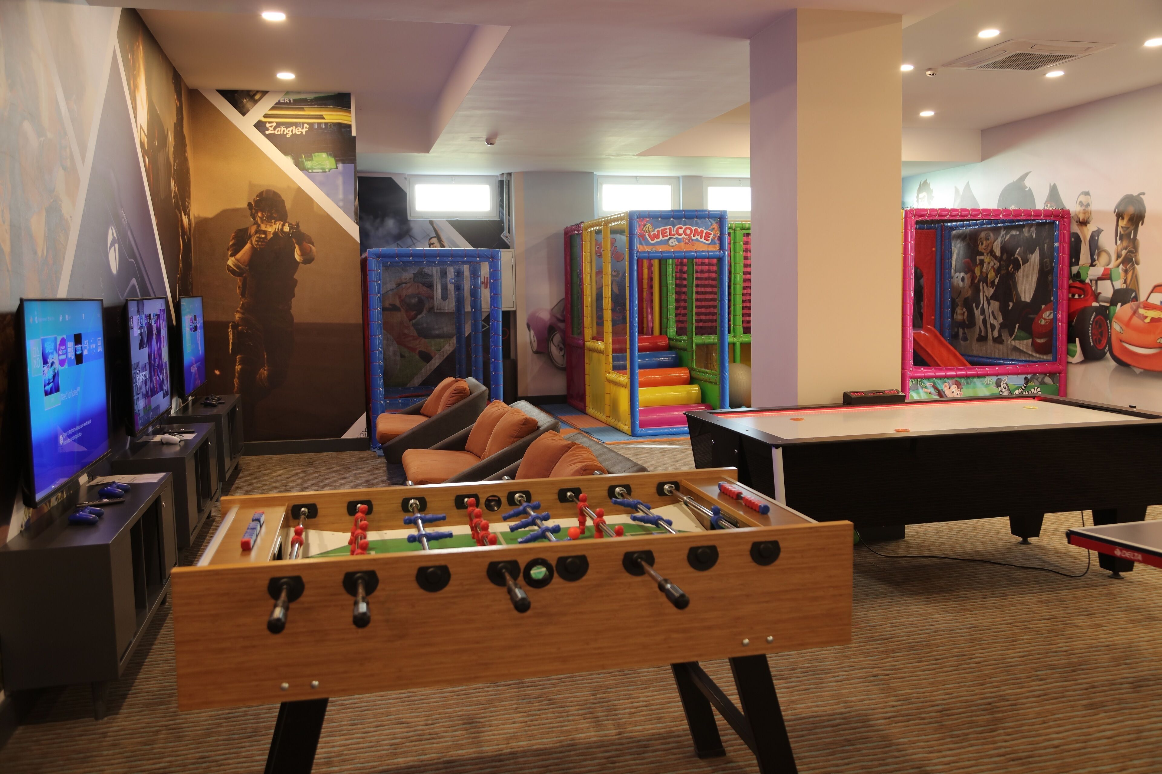 Una habitación con mesa de fútbol, mesa de billar y zona de juegos con estructuras coloridas.