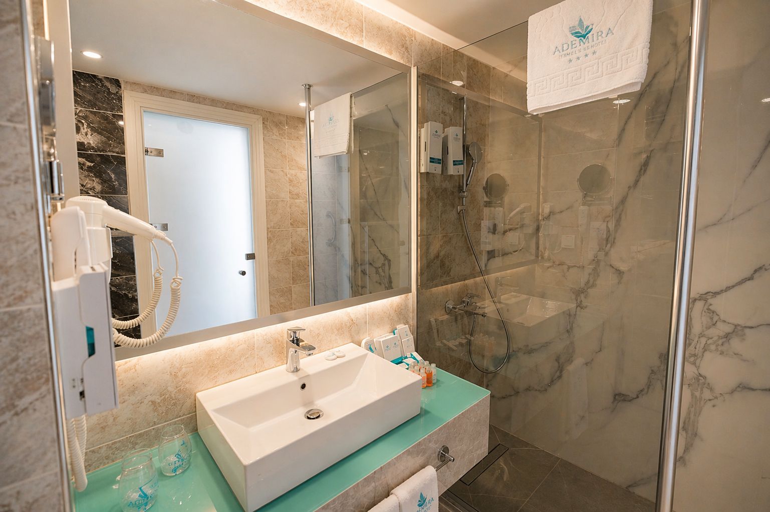 Un baño moderno con un espejo grande, un lavamanos blanco y una cabina de ducha de vidrio.