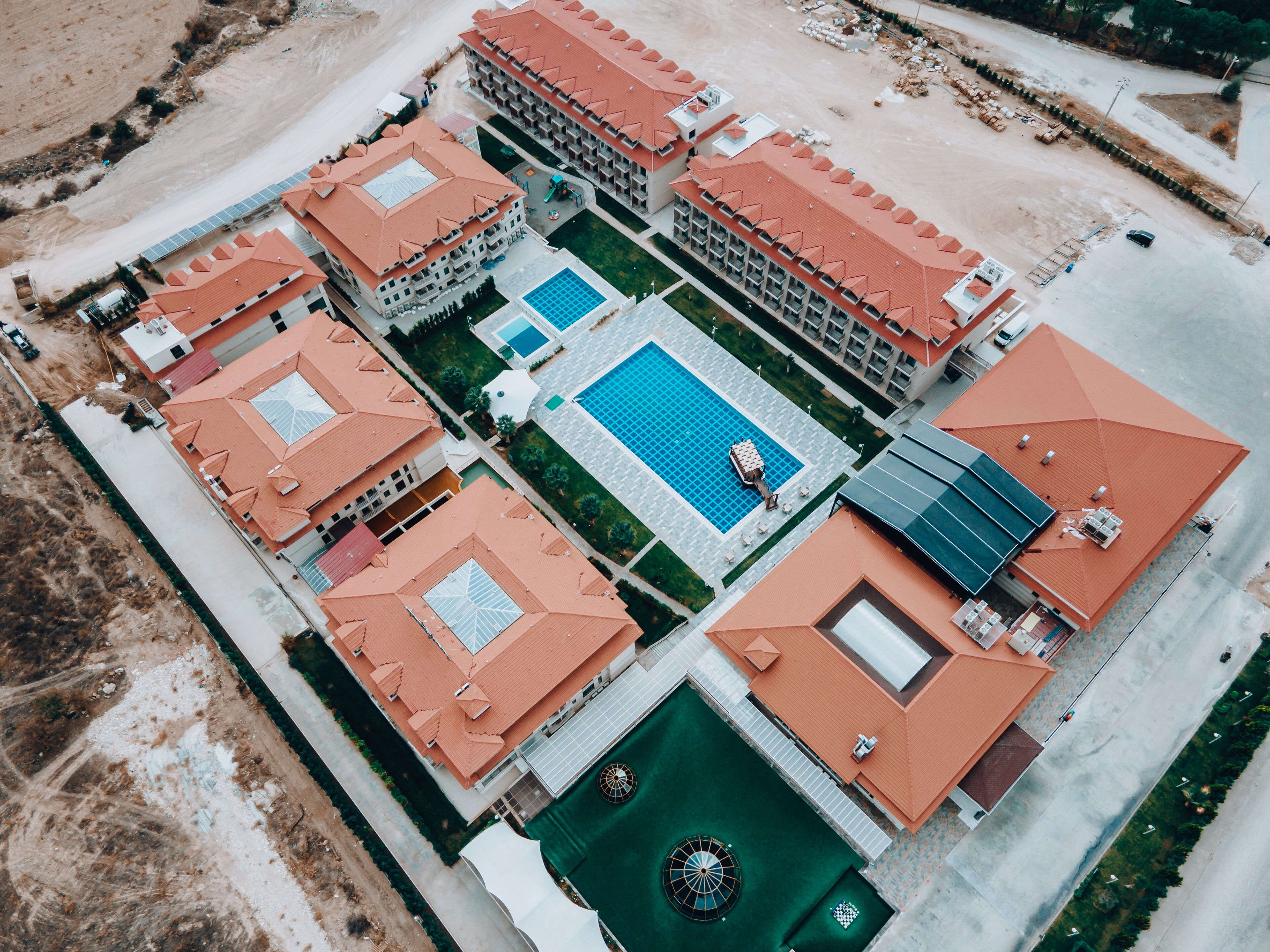 An aerial view of a hotel with multiple buildings, a central swimming pool, and surrounding landscaped areas.