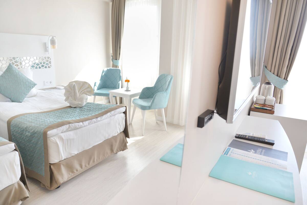 Habitación de hotel con una cama, dos sillas, una mesita y un escritorio con una computadora y control remoto.