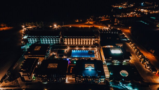 An aerial view of a hotel with multiple buildings, a swimming pool, and a well-lit parking area.