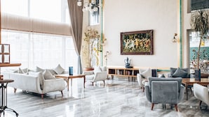 A spacious living room with a marble floor, a large window with curtains, and a painting on the wall.