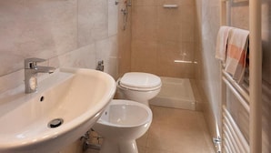 A modern bathroom with a sink, toilet, and shower. There are lights above the mirror and a small window above the toilet. - Hotel Aurelia (Tarquinia)