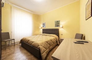 A hotel room with a bed, a desk, two chairs, and a window with blinds. - Hotel Aurelia (Tarquinia)