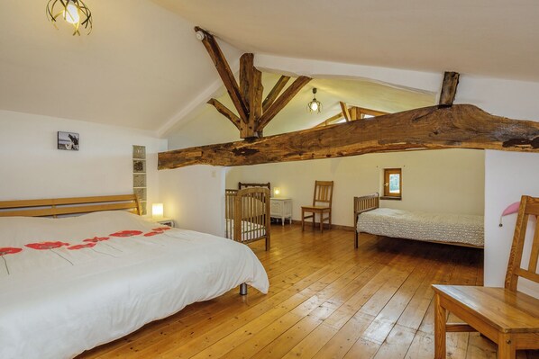 Un dormitorio con piso de madera, una cama grande con cubrecama blanco, una silla de madera y una mesita con una lámpara.