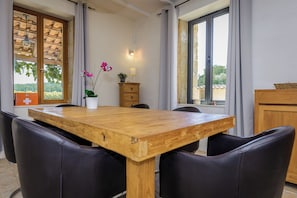 A dining area with a wooden table and black chairs, a small cabinet, and a window with a view of greenery.