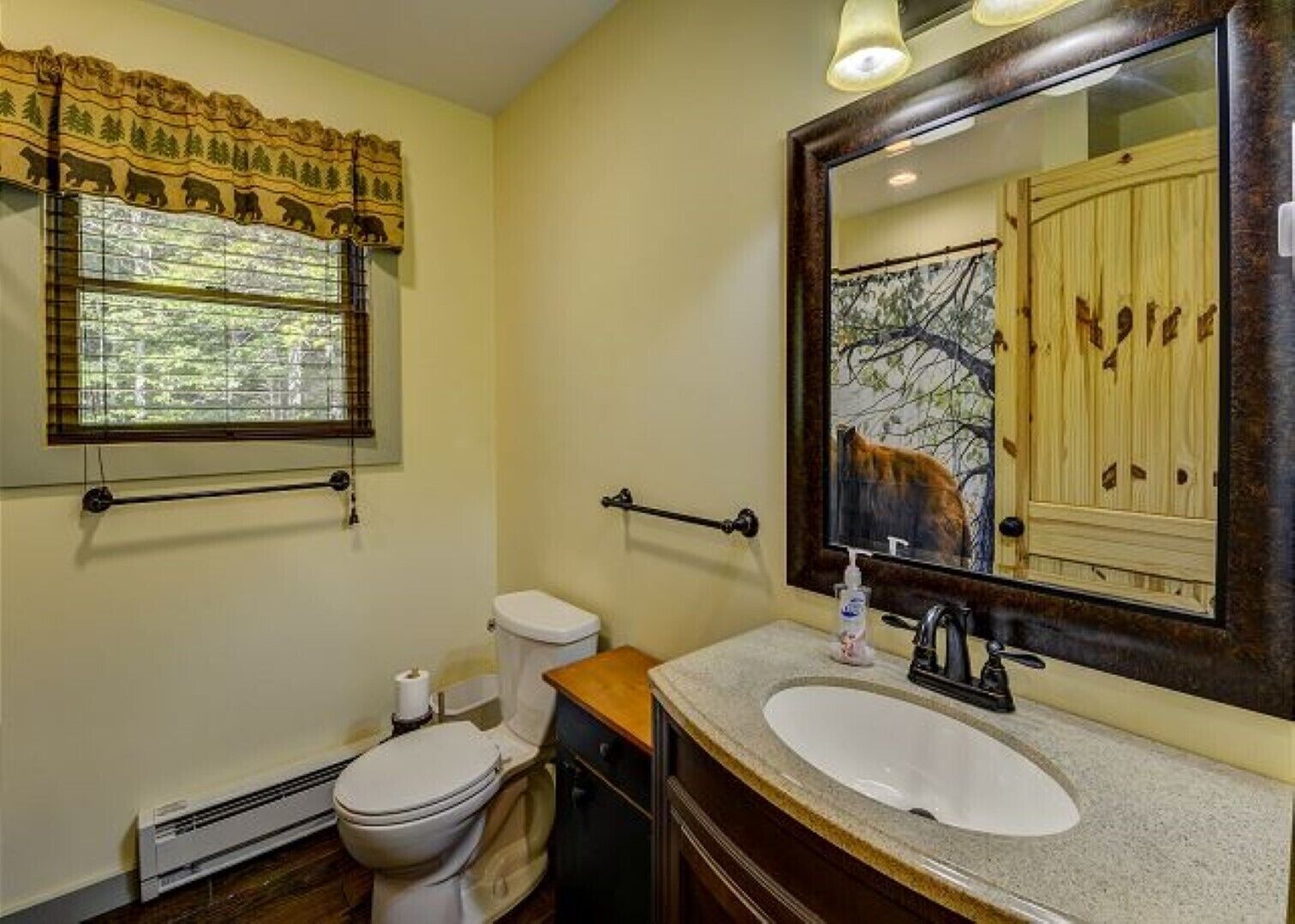 Ein Badezimmer mit Toilette, Waschbecken und einem großen Spiegel, der ein Fenster mit Blick auf Bäume reflektiert.