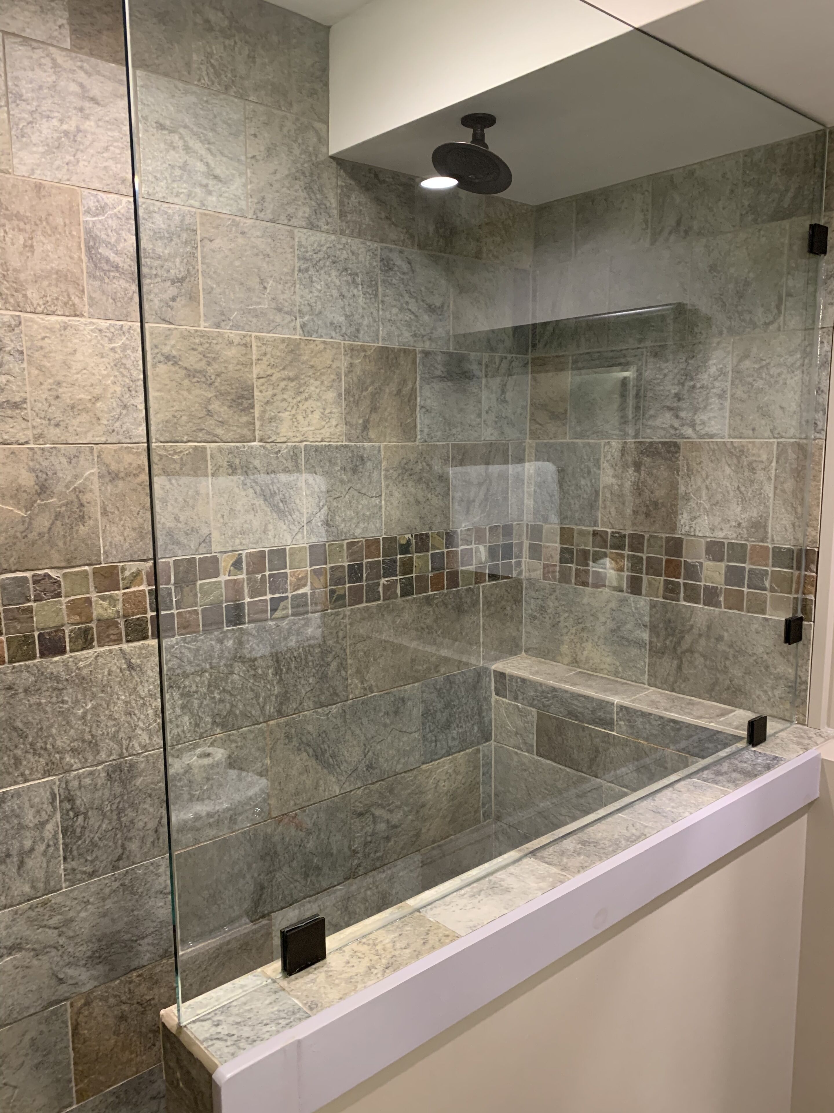 A bathroom with a glass-enclosed shower area, tiled walls, and a white countertop.