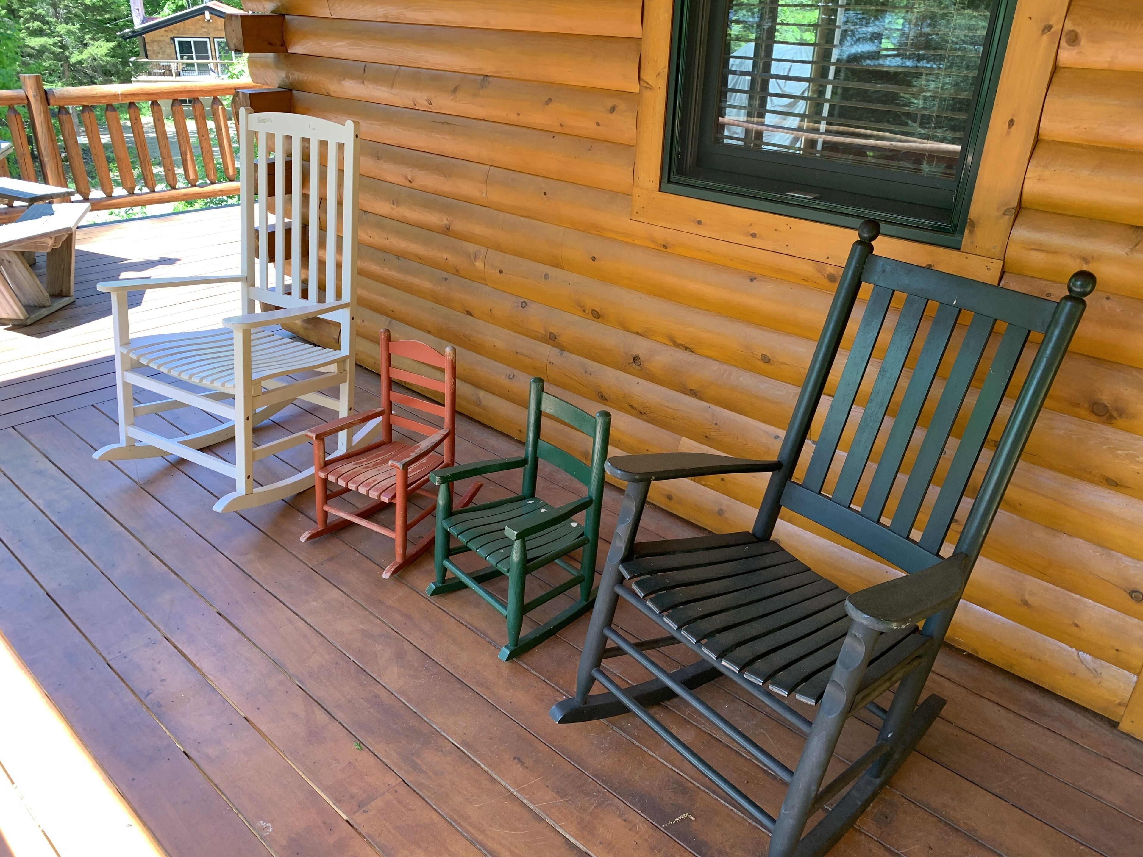 A wooden deck with three rocking chairs and a table.