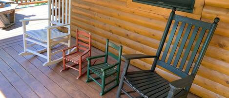 A wooden deck with three rocking chairs and a table.