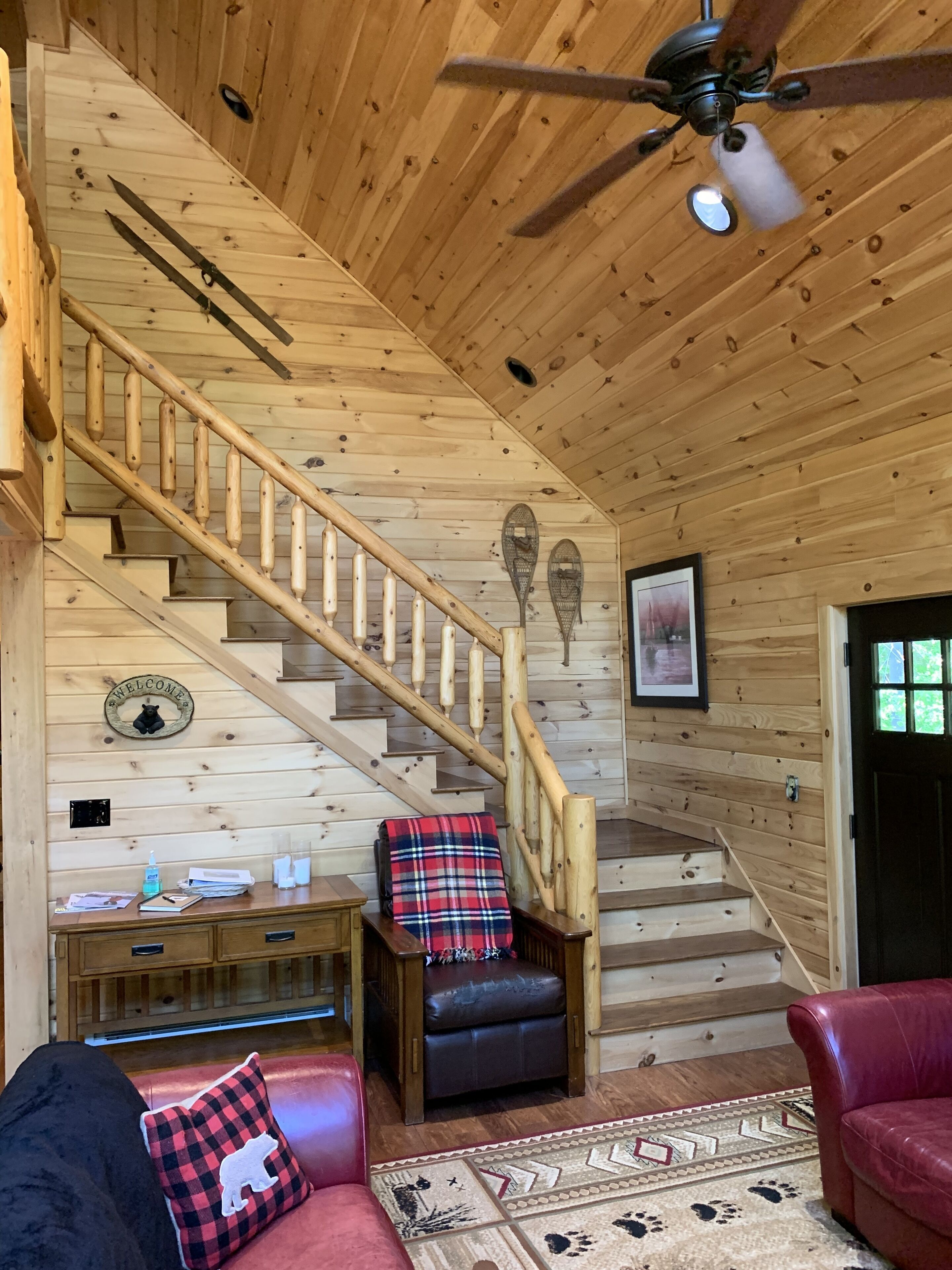 A wooden interior with a staircase, a ceiling fan, a welcome sign, a bench, and a couch.
