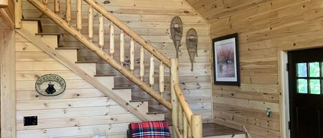 A wooden interior with a staircase, a ceiling fan, a welcome sign, a bench, and a couch.