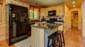 A modern kitchen with wooden cabinetry, a large island with stools, and built-in appliances. - Gorgeous 4BR Log Home Near Storyland & N. Conway. AC, Large Deck, Dog friendly (Bartlett)