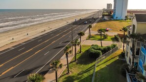 A coastal road with a beach on one side and a building with a blue facade on the other. - Poolside Retreat, Steps to the Ocean! (Galveston)
