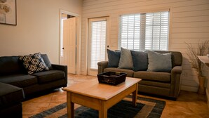 A living room with a dark brown sofa, a lighter brown sofa with blue cushions, a wooden coffee table, and a wicker plant. - Poolside Retreat, Steps to the Ocean! (Galveston)