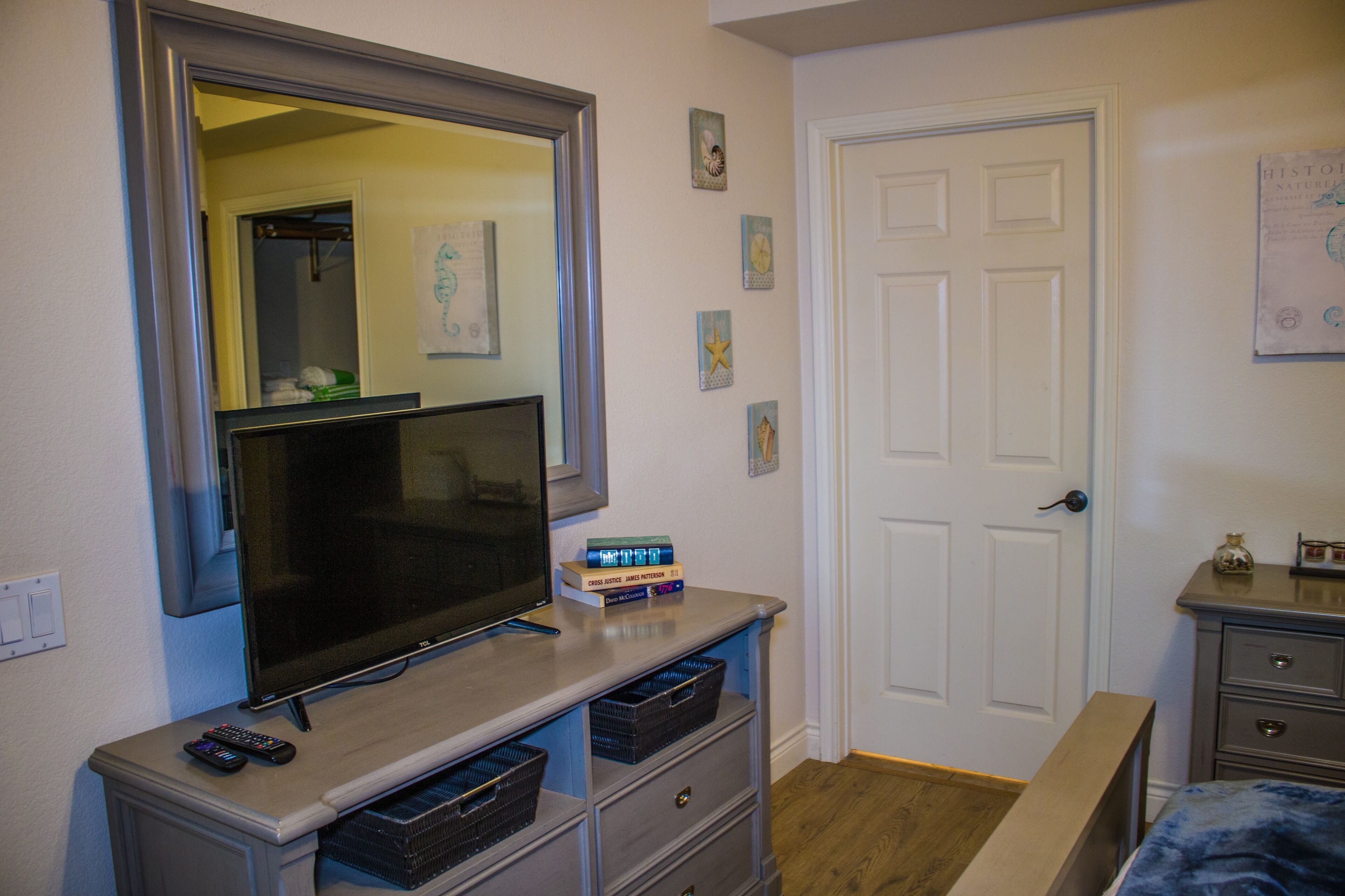 A bedroom with a TV, a dresser, a door, and a small table.